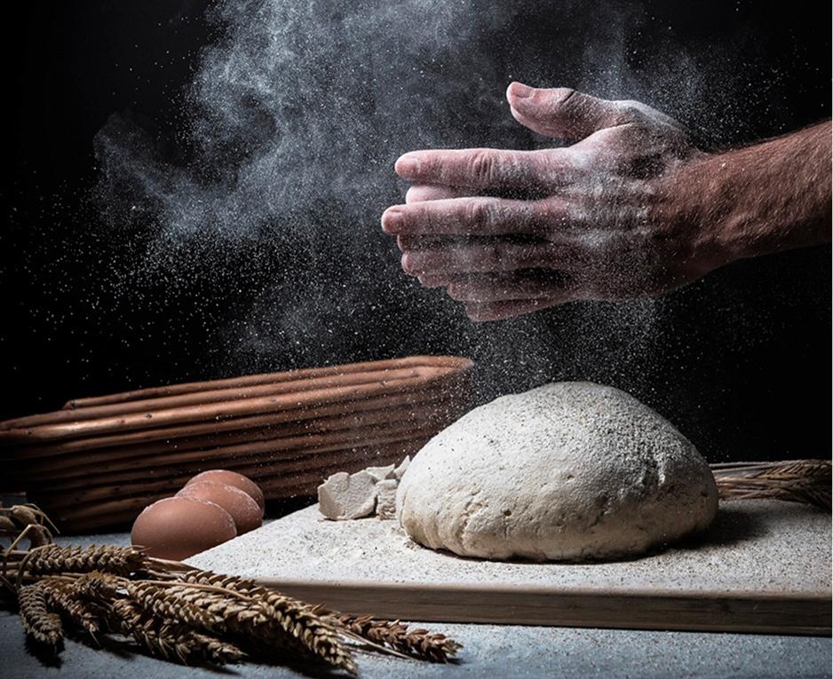 Hands preparing dough with flour, bread ingredients and wheat on a dark background.