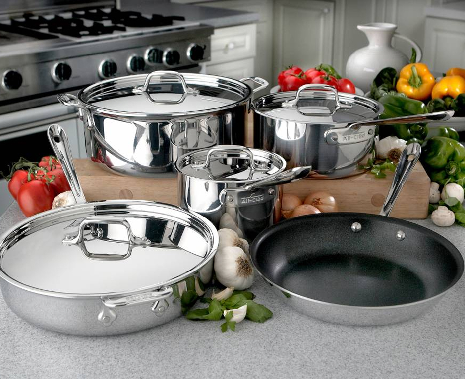 Stainless steel cookware set arranged on a kitchen countertop, surrounded by fresh vegetables.