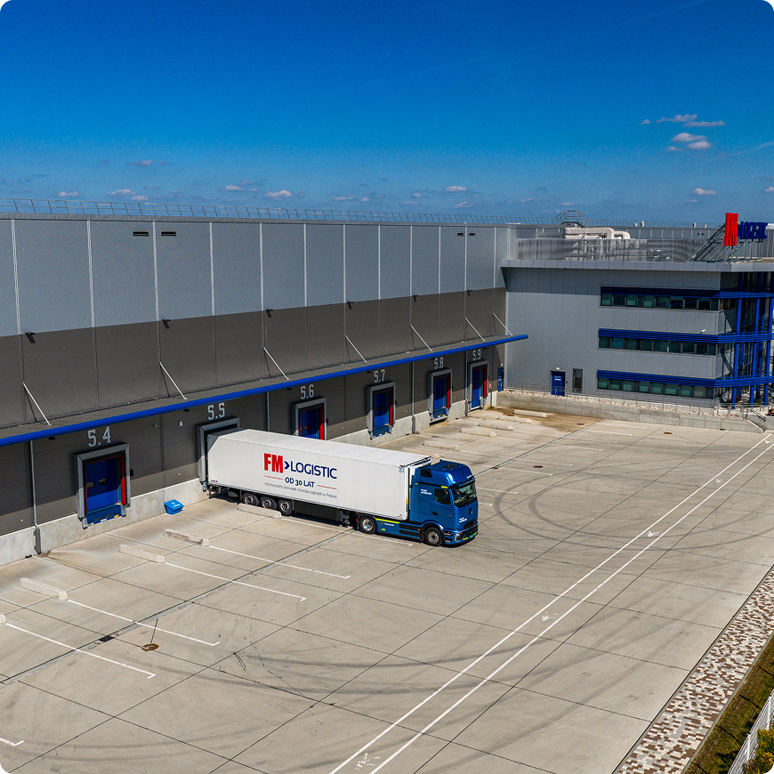 FM Logistic truck parked at a loading dock outside a logistics warehouse.