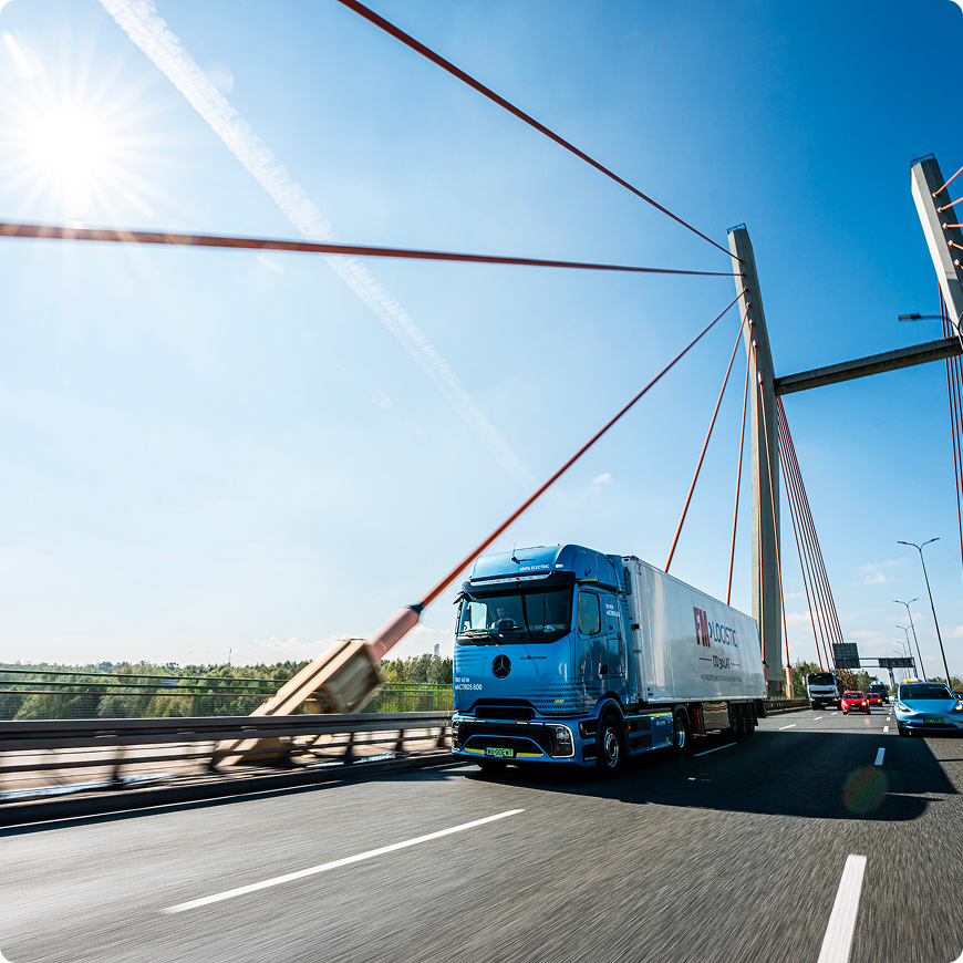FM Logistic truck driving across a cable-stayed bridge on a sunny day.