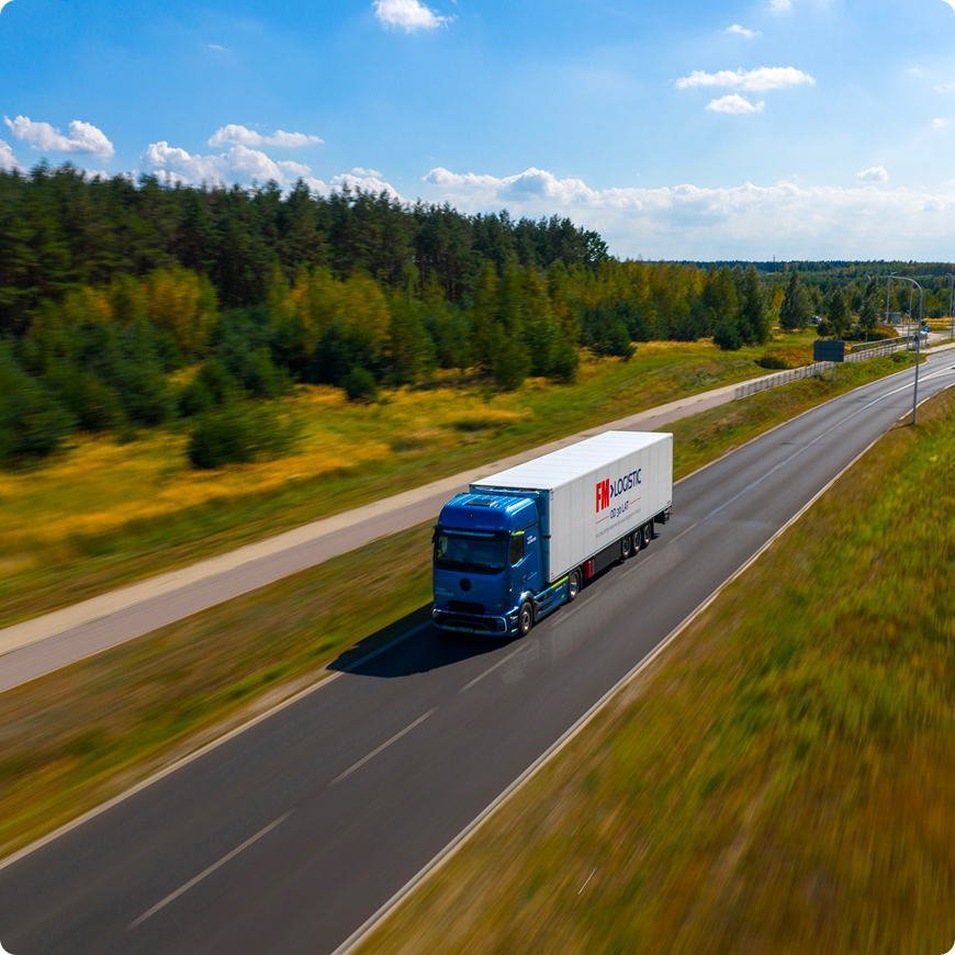 FM Logistic truck driving along a road surrounded by forest.