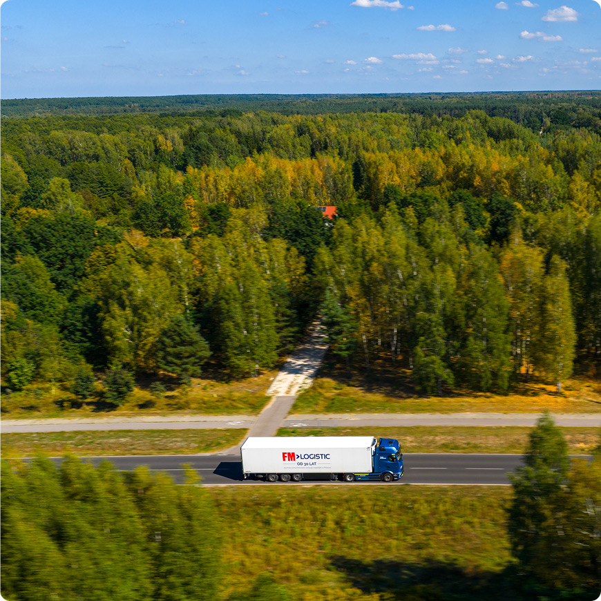 Aerial view of an FM Logistic truck driving through a forested landscape.