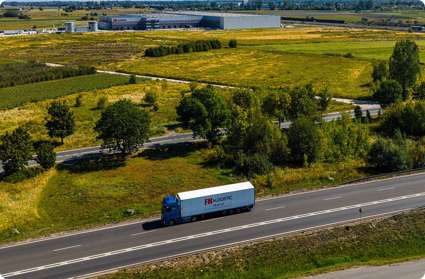 FM Logistic truck driving past a logistics facility in a green landscape.